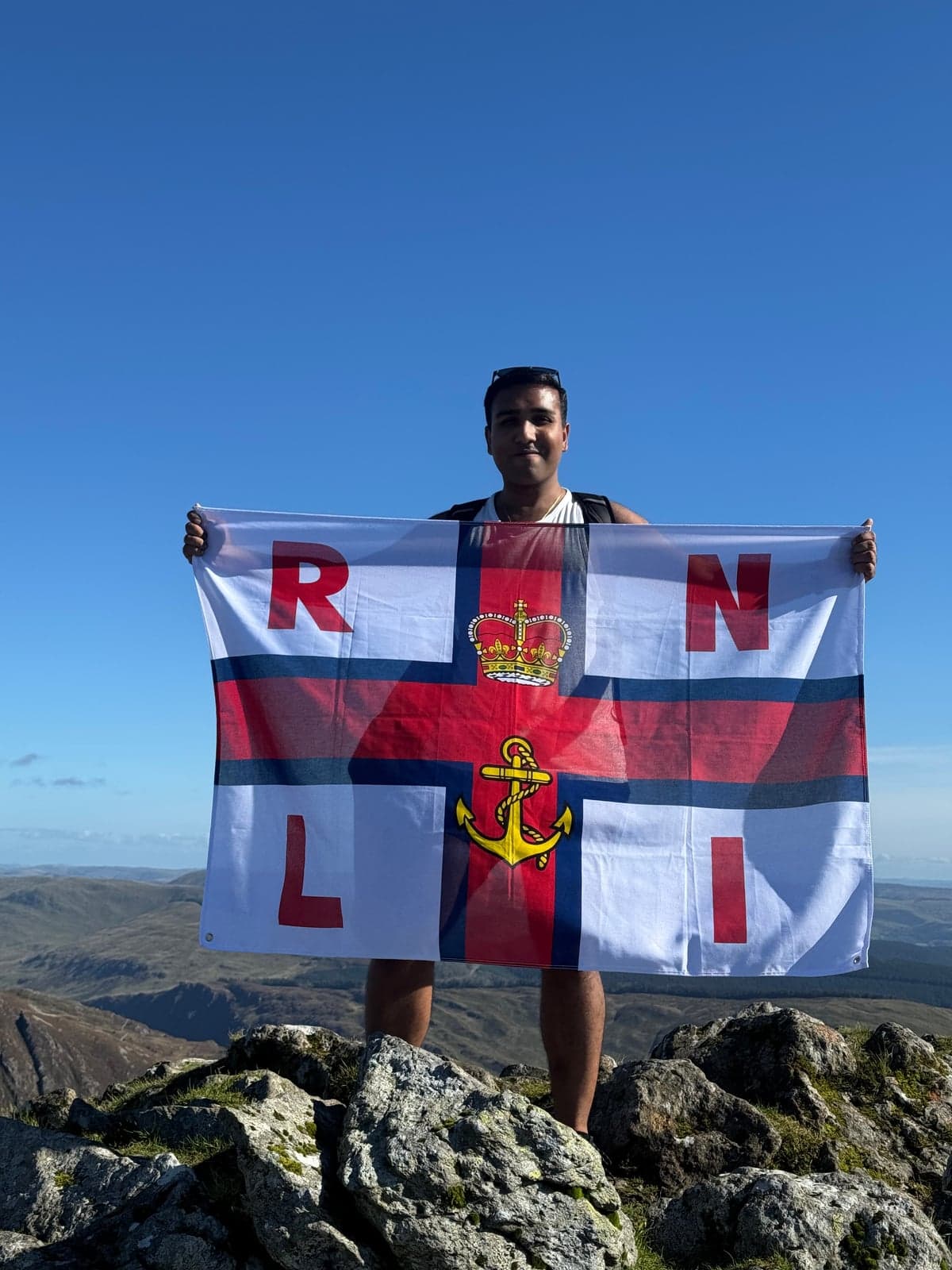 Cyng Nishant Chandolia yn dal baner yr RNLI ar Fynydd Moel